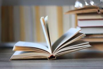 Stack of books on the table, reading glasses and e-reader on the table. Bookshelf in the background. Selective focus.