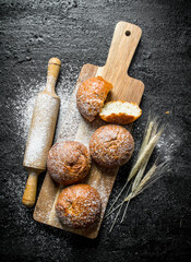 Fresh buns on a wooden cutting Board with a rolling pin and spikelets.