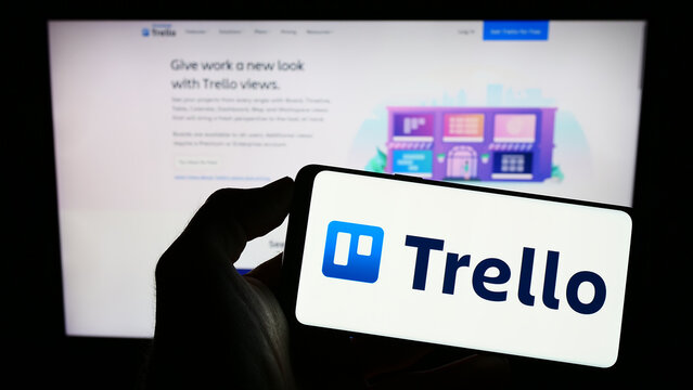 Stuttgart, Germany - 01-13-2023: Person holding mobile phone with logo of list-making software Trello on screen in front of company web page. Focus on phone display.