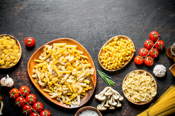 Assortment of different types of raw pasta with mushrooms, tomatoes and garlic.