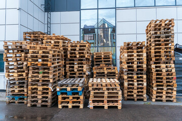 A stack of wooden pallets in an internal warehouse. An outdoor pallet storage area under the roof next to the store. Piles of Euro-type cargo pallets at a waste recycling facility.