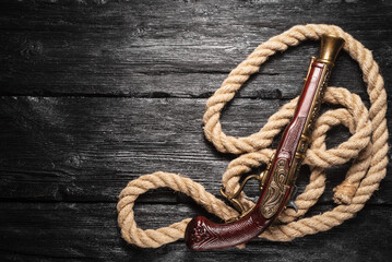 Pirate concept background. Musket gun and mooring rope on the black wooden table flat lay...