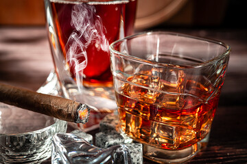 A glass of scotch whiskey with ice and a cigar on a wooden table close-up.