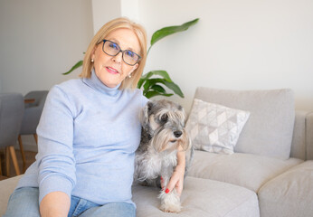 Cheerful senior woman in casual clothing spending time with her dog while sitting on the sofa at home