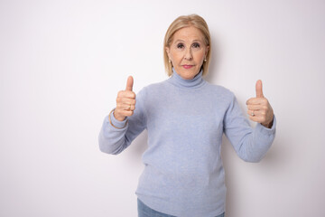 Senior woman over white background doing happy thumbs up gesture with hand. Approving expression looking at the camera showing success.