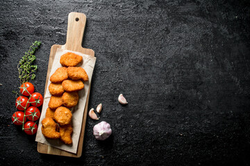 Chicken nuggets on a cutting Board with paper, cherry, garlic and thyme.