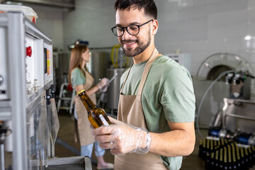 Male brewer working in a brewery filling bottles with beer.
