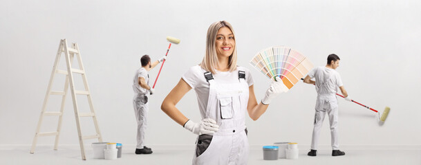 Female house painter holding a color palette and male workers painting a wall
