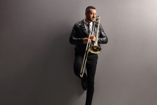 Young male trombone player standing and leaning on a wall