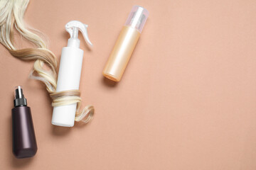 Spray bottles with thermal protection and lock of blonde hair on beige background, flat lay. Space for text
