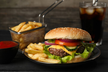 Delicious burger, soda drink and french fries served on black table