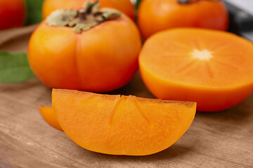 Whole and cut delicious ripe persimmons on wooden table, closeup