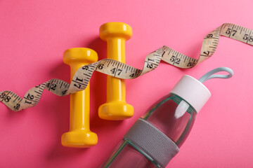 Measuring tape, bottle of water and dumbbells on pink background, flat lay. Weight control concept