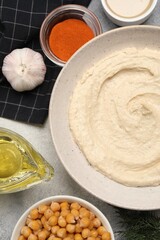 Bowl with delicious hummus and different ingredients on light grey table, flat lay