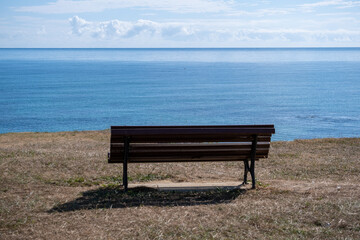 Naklejka na ściany i meble Old brown bench having a view over the sea.