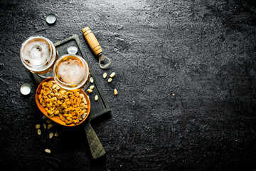 Two glasses of beer and peanuts in a bowl on a black cutting Board.