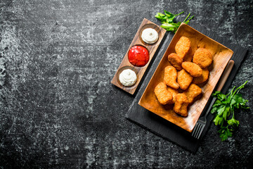 Chicken nuggets on a plate with greens and different sauces.