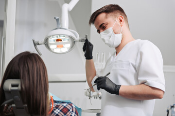 Dentist in mask and uniform consulting his patient in dental clinic.