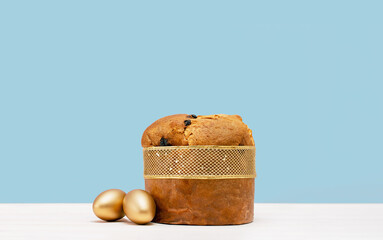Happy Easter banner. Italian Easter Decorated Panettone and golden eggs on white table. Wide banner on blue.
