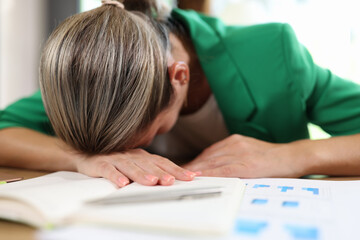 Tired and stressed woman lying on documents in her office.