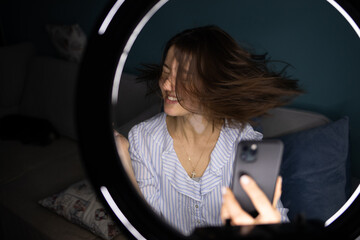 Fototapeta premium Young beautiful woman with vitiligo shoot on mobile phone with ring lamp on blue background