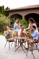 Group of young people cheering with cider and eating pizza by the pool in the garden