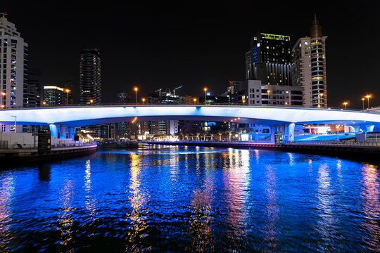 view of footbridge with tourists leading to numerous skyscrapers with hotels and residential buildings on the Persian Gulf coast in Dubai at night