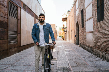 Fototapeta na wymiar Young man in denim jacket pushing his vintage classic bicycle through the alleys of the city.