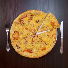 Delicious fresh cheese pizza with ham, sausage, tomatoes on black table, on white plate, fork, knife nearby, top view