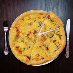 Delicious fresh cheese pizza with mushrooms, pickles, sausage on black table, white plate, fork, knife nearby, top view
