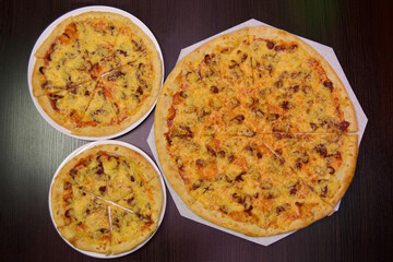 Three delicious fresh cheese pizzas with mushrooms, smoked sausages on black table, three different sizes for serving