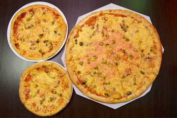 Three delicious fresh round cheese pizzas with mussels on a black table, surface, on a white plates, three different sizes for serving in a pizzeria