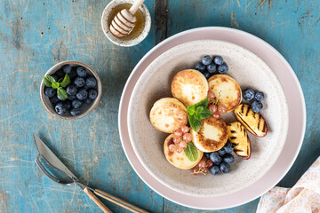 Cottage cheese pancakes, cheesecakes, ricotta fritters with fresh blueberries, currants and peaches on a plate. Healthy and delicious breakfast for the holiday. Blue wooden background