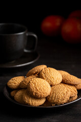 Close up of cookies, cup of coffee and tangerines on dark table, selective focus, black background, vertical, with copy space