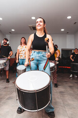 A girl plays the drum in a batucada class with a smiling attitude