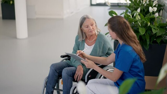 Young woman doctor talking with senior woman at wheelchair.