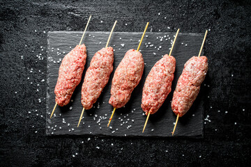 Raw kebab of ground beef on a stone Board with pieces of salt.