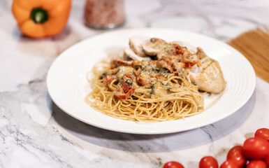 Dinner plate on the table. Gourmet Pasta with sause and sundried tomatoes. Chicken on the side.