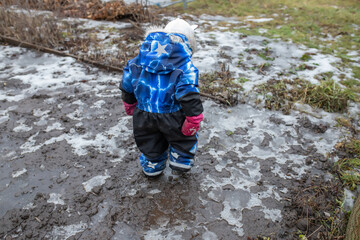 The child walks off-road with melting snow and mud after a thaw in the spring.