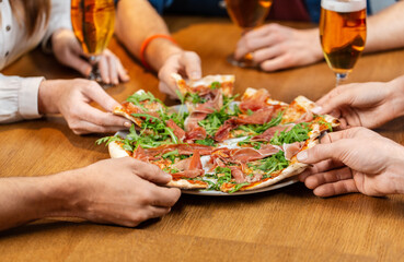 Obraz na płótnie Canvas leisure, food and drinks, people and holidays concept - close up of friends eating pizza and drinking beer at restaurant or pub