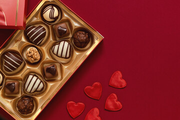 Gift box with chocolate candies and red heart decoration for Valentine's Day on a burgundy background. Top view. Copy space.