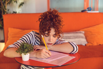 Young girl writing something and looking tired and bored