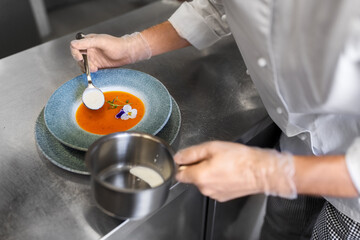 food cooking, profession and people concept - close up of chef serving plate of pumpkin cream soup...