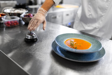 food cooking, profession and people concept - close up of male chef with plate of pumpkin cream soup ringing bell at restaurant kitchen table