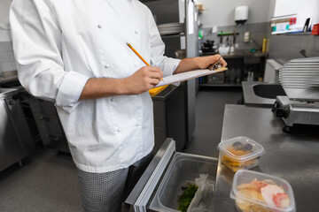 restaurant business, profession and people concept - close up of male chef with clipboard doing inventory in kitchen fridge