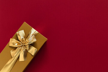 Golden gift box with golden ribbon and bow on a burgundy background. Top view. Copy space.