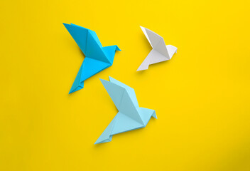 Origami art. Colorful handmade paper birds on yellow background, flat lay
