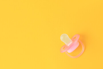 One new baby pacifier on orange background, top view. Space for text