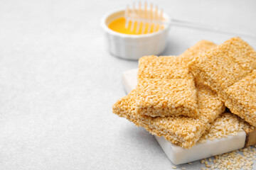 Delicious sesame kozinaki bars and honey on white table, closeup. Space for text