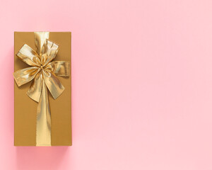 Golden gift box with golden ribbon and bow on a pink background. Top view. Copy space.